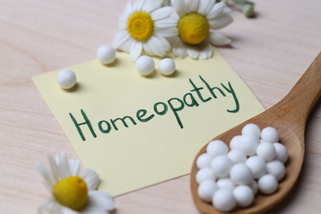Sticky note with word Homeopathy, pills and chamomile flowers on wooden table, closeup Was ist Osteopathie? - Bach